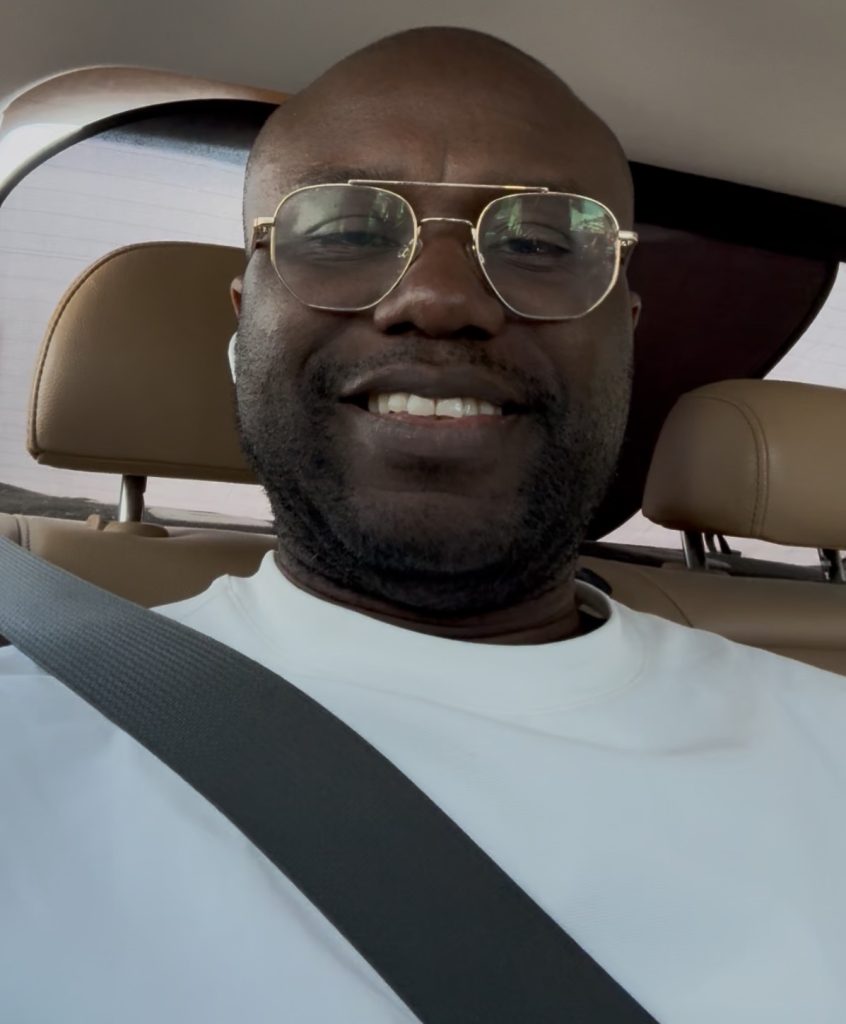 Close-up of smiling man wearing glasses in a car, with a seatbelt across his chest
